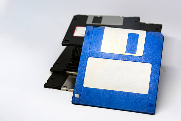 een blauwe diskette met een wit plakkerig label met een stel andere zwarte diskettes op de achtergrond. Verouderde technologie voor gegevensopslag. - Foto, afbeelding