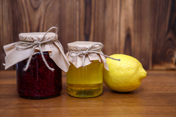 Prevention for colds, flu. Raspberry jam, honey and lemon on a wooden background, space for text. - Fotó, kép