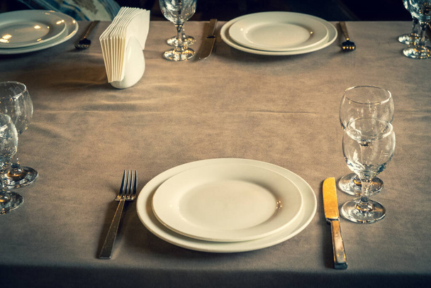 Der servierte Tisch im Restaurant. Reinigen Sie Geschirr und Geräte auf der Tischdecke in einem Café. Glänzend transparente Gläser. Weiße Teller vorhanden. Vorbereitet für den Empfang der Gäste. Hoher Service. - Foto, Bild