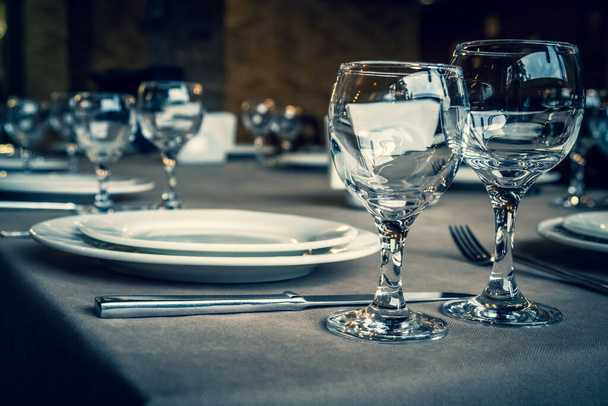 The served table in the restaurant. Clean dishes and appliances on the tablecloth in a cafe. Shiny transparent glasses. White plates. Prepared for the reception of guests. High service. - Photo, Image