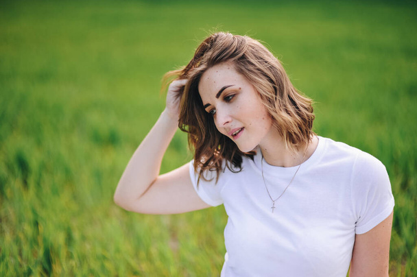 The girl is blonde, brown hair, in a white shirt and blue midi skirt. Walking in the field, through the green grass. Portrait of a girl. Positive and smile. - Photo, image