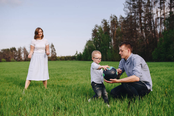 Rodina v lese na procházku. Piknik na louce, na zelené trávě. Modré šaty. Mami, tati, syn hrají fotbal. Zvíře. Černý pes. Chlapec s brýlemi. - Fotografie, Obrázek