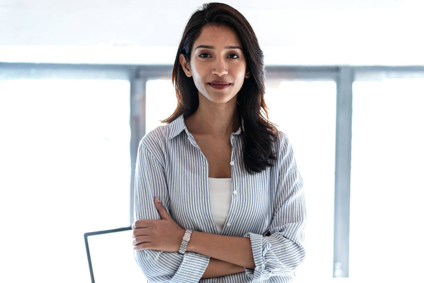 Shot of elegant young business woman looking at camera while standing in the office. - Foto, afbeelding