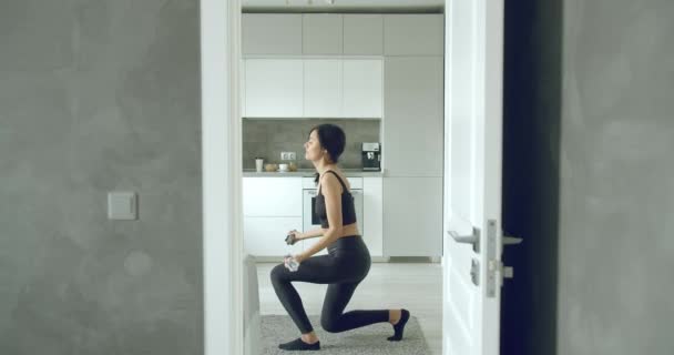 Young athletic woman doing exercises with dumbbells at home. Sports and training during self-isolation - Materiaali, video