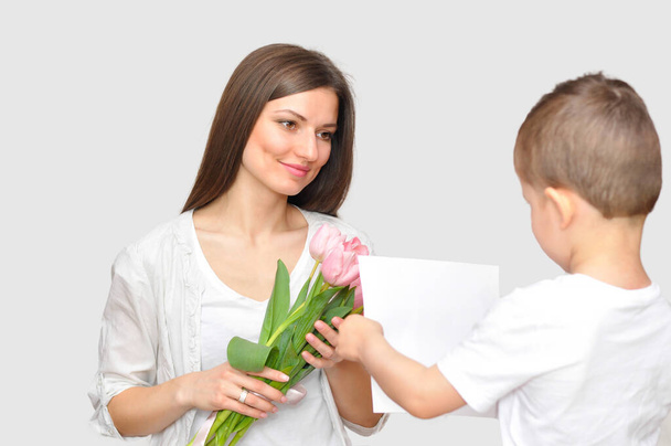 Ο μικρός γιος δίνει στη μητέρα του ένα μπουκέτο λεπτές ροζ τουλίπες. Γιορτή της Μητέρας. - Φωτογραφία, εικόνα