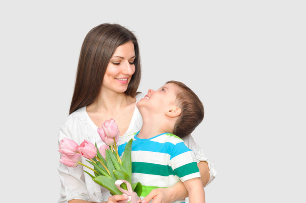 Ο μικρός γιος δίνει στη μητέρα του ένα μπουκέτο λεπτές ροζ τουλίπες. Γιορτή της Μητέρας. - Φωτογραφία, εικόνα