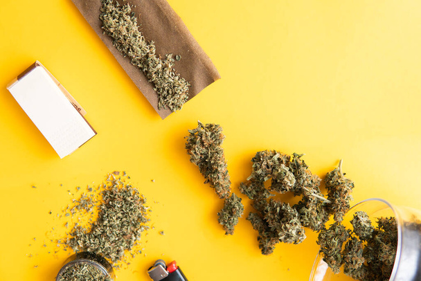 Background for Copy space. Hemp legalisation. Fresh marihuana. Top view. Cannabis buds on yellow background. CBD and THC on buds in cannabis. Blunt and Lighters. - Photo, Image