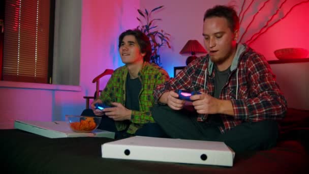 Zwei befreundete junge Männer spielen mit Gamepads und haben Spaß - Filmmaterial, Video
