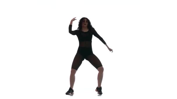 νεαρή όμορφη κοπέλα σε ένα μαύρο διαφανές σφιχτό κοστούμι ενεργειακά χορό dancehall, street dance, twerk σε λευκό φόντο, απομονωμένη  - Πλάνα, βίντεο