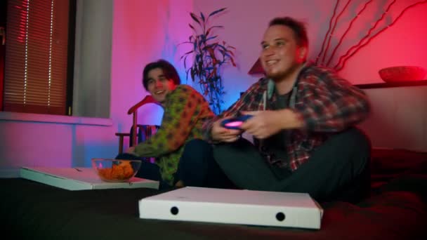 Dwóch młodych mężczyzn przyjaciele siedzi na łóżku i gra z gamepads i zabawy - Materiał filmowy, wideo