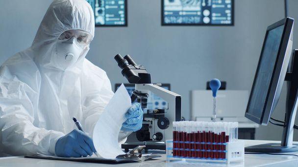 Scientist in protection suit and masks working in research lab using laboratory equipment: microscopes, test tubes. Coronavirus 2019-ncov hazard, pharmaceutical discovery, bacteriology and virology - Photo, Image