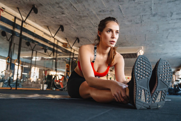 Portrait of athletic beautiful sportswoman stretching her leg while working out in athletic hall - Foto, afbeelding