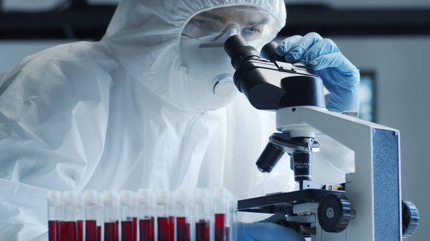 Wissenschaftler in Schutzanzügen und Masken arbeiten im Forschungslabor mit Laborausrüstung: Mikroskope, Reagenzgläser. Coronavirus 2019-ncov hazard, pharmazeutische Entdeckung, Bakteriologie und Virologie - Foto, Bild