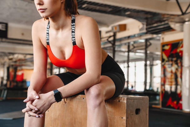 Vágott portré a sportos gyönyörű sportnő smart watch ül, miközben edz a sportcsarnokban - Fotó, kép