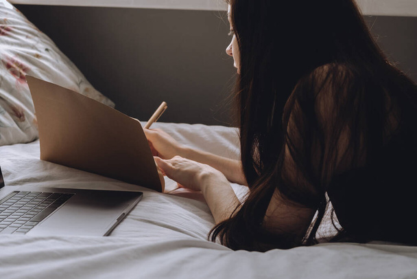 Young woman lies on bed with laptop and notebook. - Foto, immagini