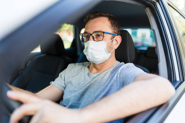 Portrait of man wearing surgical mask while driving a car. - Foto, Bild