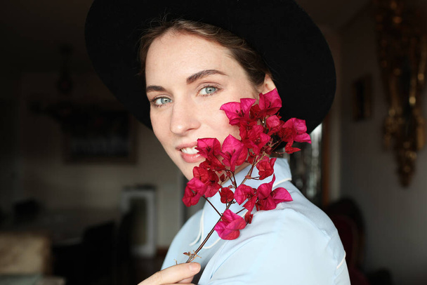Side portrait of young woman have a emotional face and good mood and wearing hat and holding wildflowers. - Фото, изображение