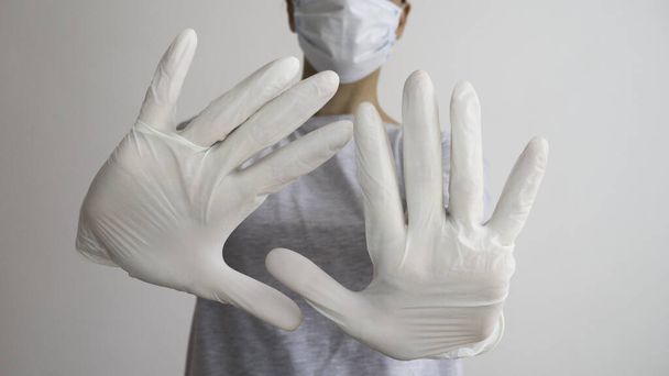 医療用マスクと白いラテックス手袋を持つ女性は、シンボルを示しています両手で停止. - 写真・画像