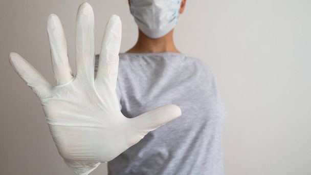 医療用マスクと白いラテックス手袋の手を持つ女性は、シンボルSTOPを示しています。病気を止めなさい. - 写真・画像