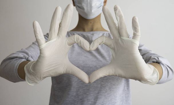 Vrouw met een medisch masker en handen in latex witte handschoenen toont het symbool van het hart. Dokter voor het hart. Liefde voor onze alvleesklier. Hou van onze medische professionals. - Foto, afbeelding