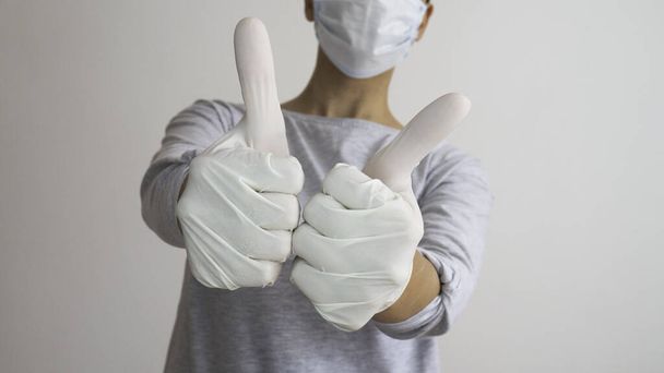 A female with a surgical mask and white rubber gloves gives thumbs up with both hands. - Photo, Image