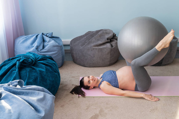 Pregnant european woman performs exercises with fitness ball. Expectant mother is doing yoga in the 3rd trimester. Girl in the classroom in preparation for childbirth. - Fotó, kép