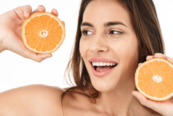 Beauty portrait of an attractive smiling young topless woman standing isolated over white background, showing sliced orange - Zdjęcie, obraz