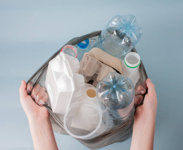 Hands hold a package with sorted waste, plastic, glass, bottles, paper, debris on a light background, close-up. The concept of ecology, waste sorting. - Fotó, kép