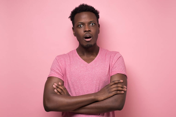 Šokovaný mladý africký Američan v růžových šatech se překvapeně dívá do kamery, ohromen zajímavým příběhem. Lidské výrazy a emoce na barevné zdi studia. - Fotografie, Obrázek