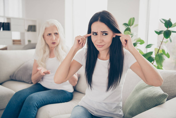 Portrait of two nice attractive lovely charming annoyed irritated women talking having fight pretense sitting on divan in light white interior room house flat apartment - Foto, immagini