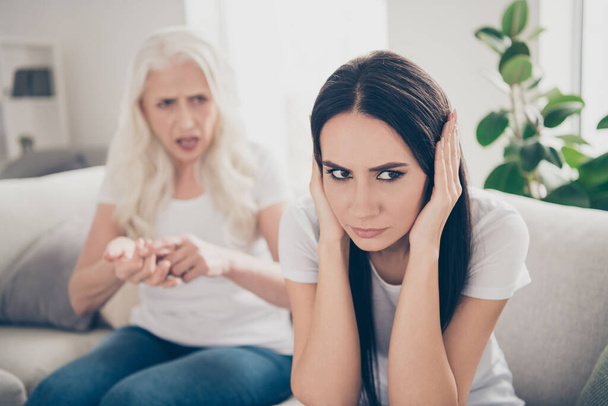 Portrait of frustrated angry young girl have disagreement misunderstanding with her old irritated mother sit couch tell talk say speak arguments she close cover her ears in house indoors - Фото, зображення