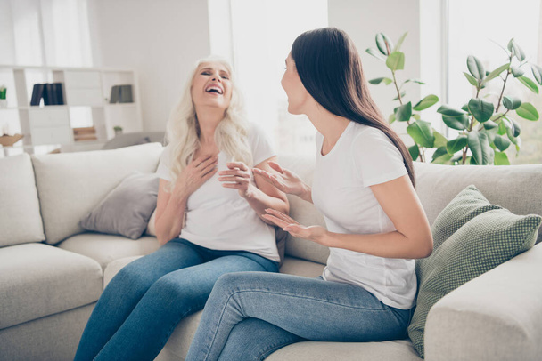 Portrait of positive cheerful grey hair brown hair women old mum girl sit couch she tell joke mom laugh in room indoors - Foto, Imagen