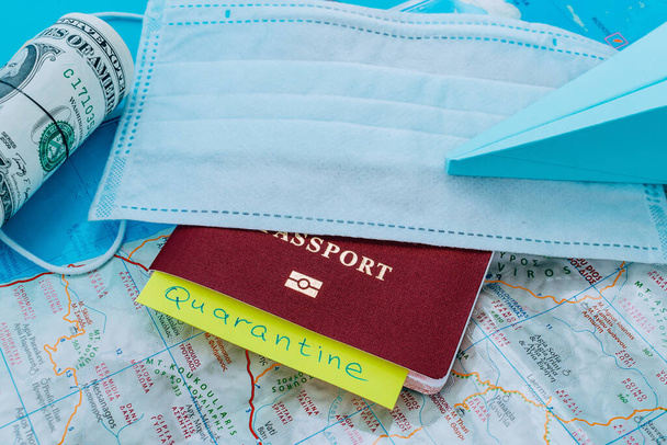 Blue paper airplane,protective mask,dollars,passport and yellow sticker with the word QUARANTINE on the background of a Greece's map.Concept of a flight ban due to coronavirus pandemic. - Foto, afbeelding
