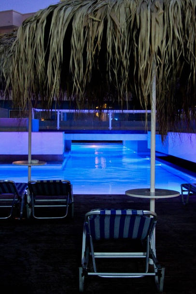 Sun beds by the pool with blue lights at night - Photo, Image