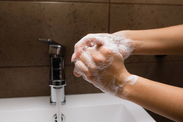 Händewaschen in einem weißen Waschbecken. Wasser fließt in seifige Frauenhände. Schutz vor Coronavirus und Infektionen. - Foto, Bild