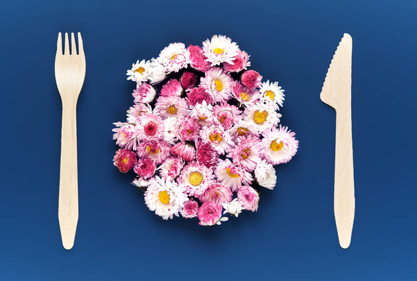 flowers in the center of the table instead of plates, next to wooden cutlery on a blue background. concept of unity with nature and environmental care - Fotografie, Obrázek