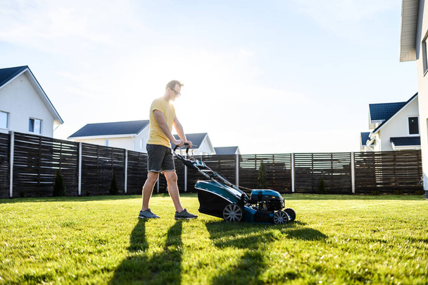 A young guy mows a lawn with a lawn mower - Φωτογραφία, εικόνα