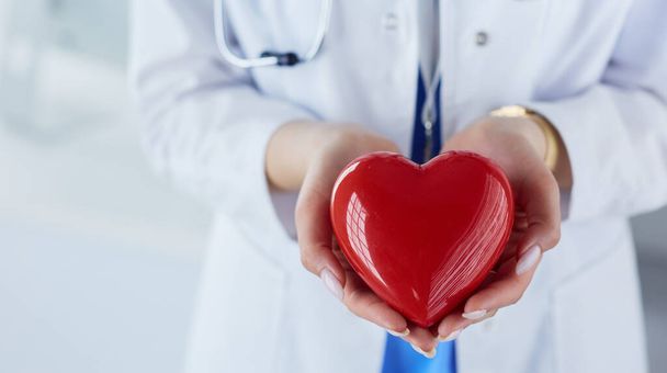 Doctora con estetoscopio sosteniendo el corazón, sobre fondo claro - Foto, imagen