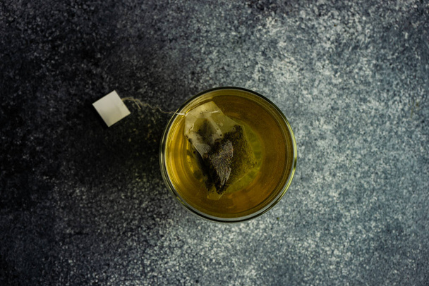 Minimalist composition with glass of green tea bag with tag on concrete background with copy space - Fotó, kép