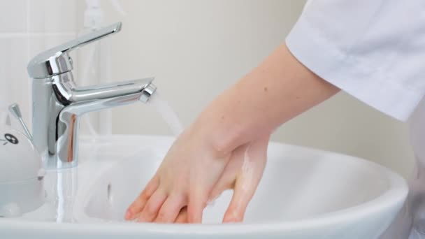 女性の医者は水の流れの下の流しで彼の手を洗い、それらを振るし、水をオフにします。閉めろ。病院における健康管理及び予防 - 映像、動画