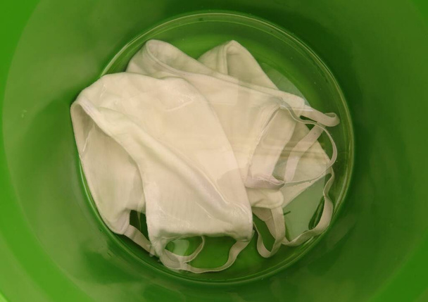 Tissue masks dipped in sanitary water solution. Coronavirus and respiratory diseases prevention. White protective masks disinfecting in green bucket Biosafety measures during pandemic  - Photo, Image