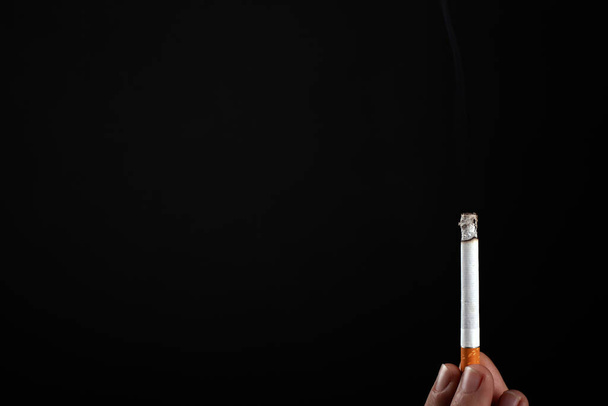 lit cigarette in hand on a black background copy space - Foto, Imagen