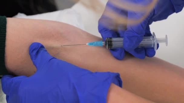 A aproximação de mãos de enfermeira insere a agulha na veia. Um médico que usa luvas de proteção azuis vai tirar sangue de uma veia de pacientes para análise. Doar sangue, salvar vidas
 - Filmagem, Vídeo
