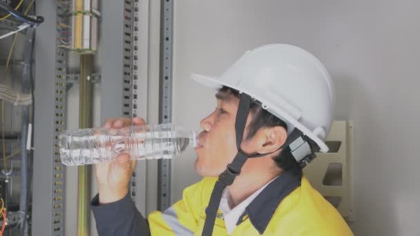 A maintenance technician is drinking water in front of the fire control cabinet. - Séquence, vidéo