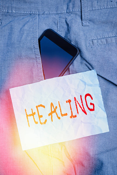 Text sign showing Healing. Conceptual photo process of making or becoming sound or healthy again Helping injured Smartphone device inside formal work trousers front pocket near note paper. - Photo, Image