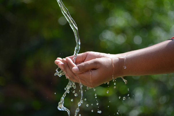 子供の手に自然を背景に水を注ぐ。水のスプラッシュと手. - 写真・画像
