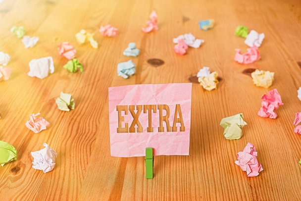 Text sign showing Extra. Conceptual photo Added to existing or usual amount number In addition normal Give more Colored crumpled papers empty reminder wooden floor background clothespin. - Photo, Image