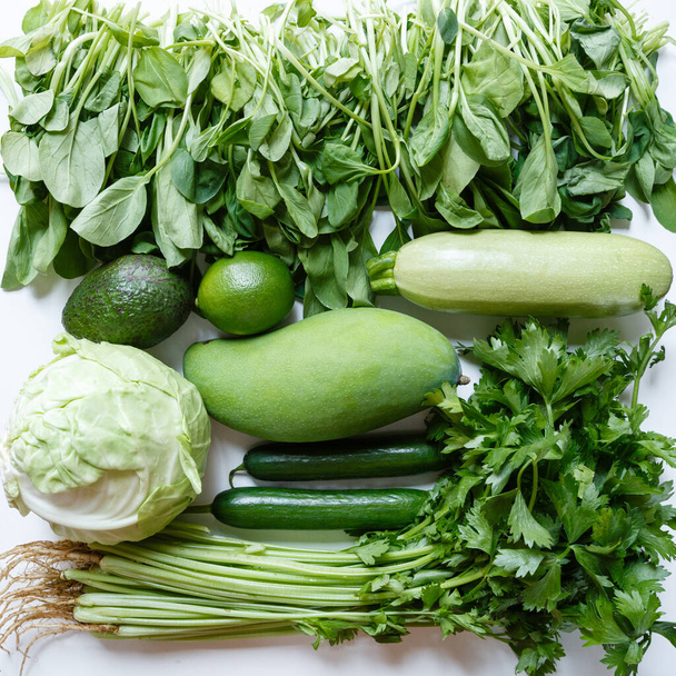 Flat lay food, fresh green vegetables and fruits: celery, cucumber, mango, lime, cabbage, spinach on white kitchen table. Top view. Healthy lifestyle and diet during coronavirus covid-19 lockdown. - Photo, image