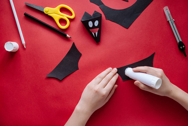 How to make bat out of paper at home. Hands making craft out of paper. Step by step photo instruction. Step 10. Glue the wings. Children DIY art project - Photo, Image