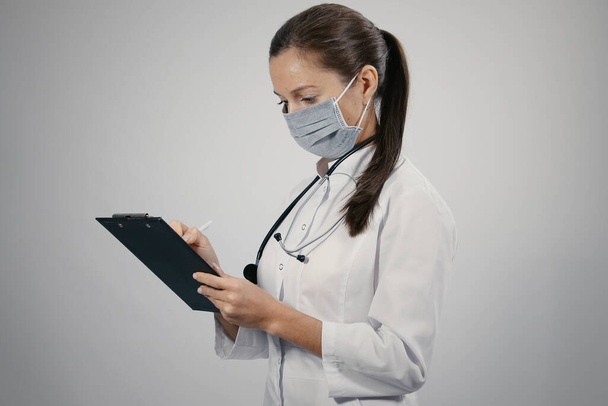 Kedves női orvos egy fehér orvosi kabát háziorvos egy fonendoszkópos írás jegyzetek, hogy a betegek kinevezések ütemezése jegyzettömbben - Fotó, kép